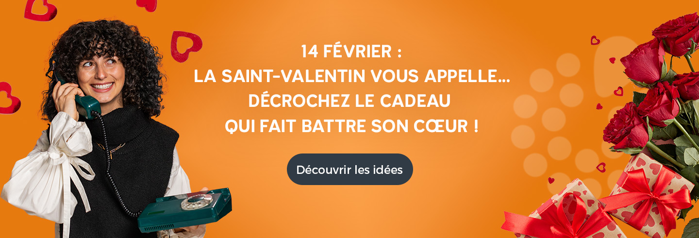 Femme souriante tenant un téléphone vintage vert sur fond orange, entourée de cœurs et de roses rouges, avec le message « 14 février : la Saint-Valentin vous appelle… décrochez le cadeau qui fait battre son cœur » et un bouton « Découvrir les idées ».